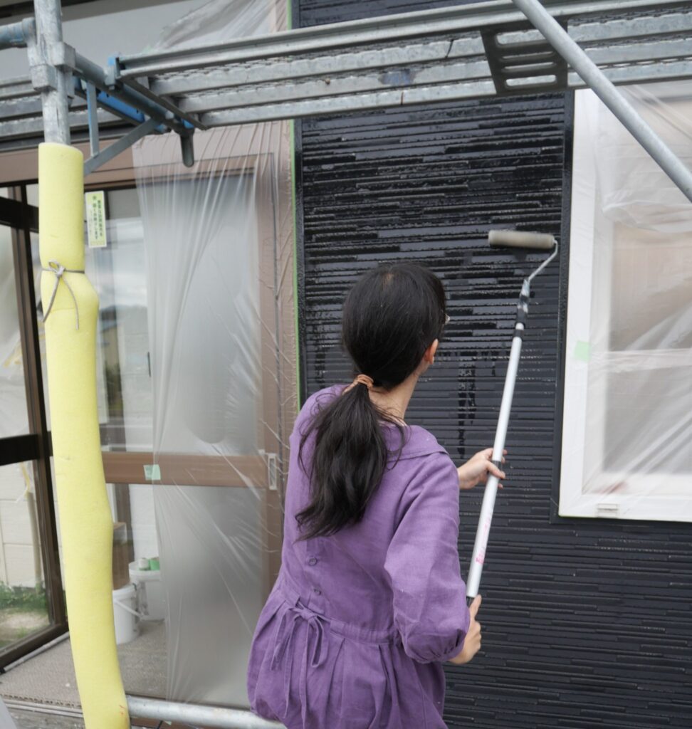 長い柄のローラーでフッ素樹脂塗装の外壁にシーラを塗る様子
